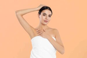 Young woman displaying smooth, hairless armpit after laser hair removal treatment against a peach-colored background